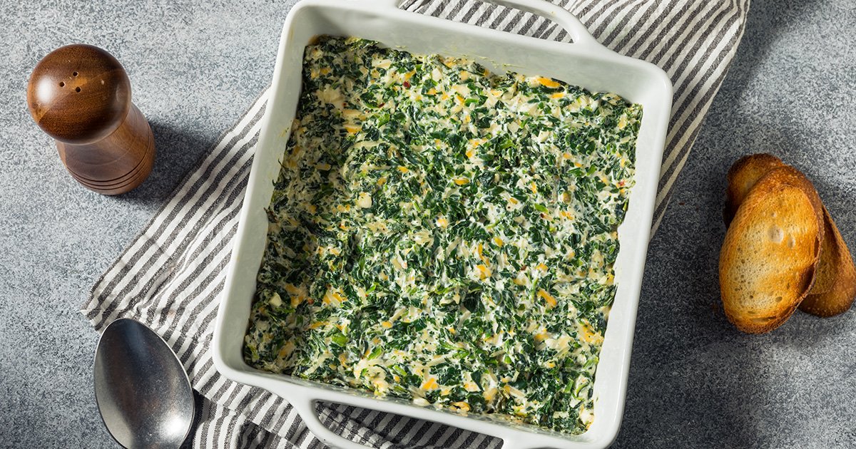 Creamy Spinach Artichoke Dip in a white square pan on a gray table